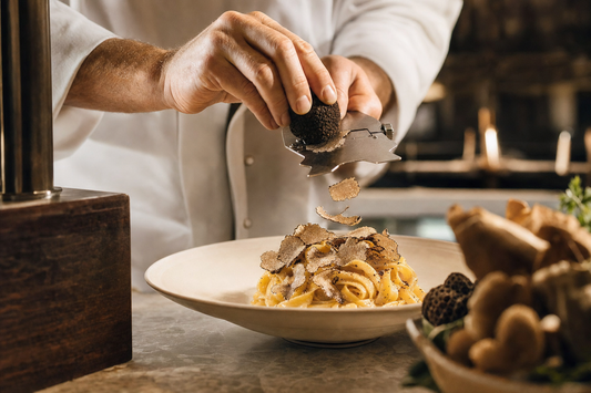 Chef shaving fresh truffle over a plated pasta dish during restaurant service